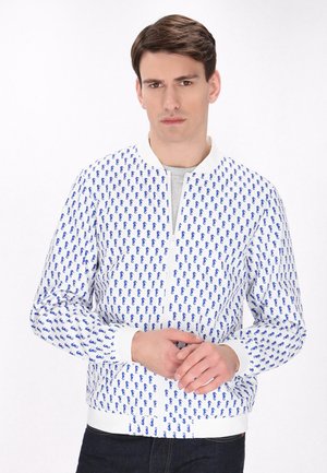 Witte bomberjack met een herhalend blauw patroon, geribde manchetten en boord, met een ritssluiting en een ronde kraagontwerp.