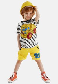 Camisa de manga corta a rayas con un gráfico de un camión amarillo, combinada con pantalones cortos amarillos brillantes que tienen el número 93 en azul. Zapatillas altas naranjas.