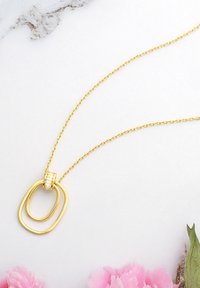 Guldkæde med sammenflettede ovale former, hvor den ene er lidt større end den anden, og med en dekorativ cubic zirconia accent.