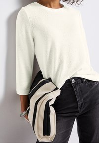 Pull en maille gris clair à manches trois quarts, associé à un jean noir. La tenue comprend un sac rayé noir et crème.