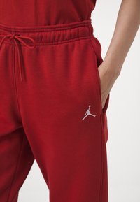 Rote Sweatpants aus weichem Stoff, mit elastischem Bund und Kordelzug, seitlichen Taschen und einem weißen Jordan-Logo am Oberschenkel.