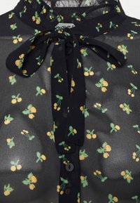 Svart genomskinlig blus med en slipskrage; har ett tryck av gula och gröna körsbär, knappstängning och texturerad tyg.