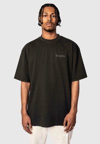 Black oversized t-shirt made of cotton, featuring short sleeves and a small, embroidered logo on the chest. Simple, clean design.