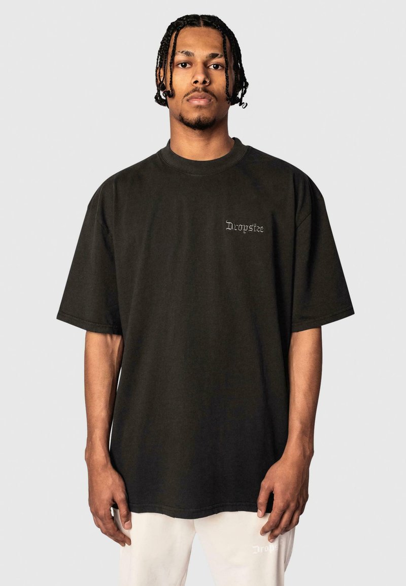 Black oversized t-shirt made of cotton, featuring short sleeves and a small, embroidered logo on the chest. Simple, clean design.