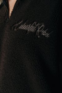 Pullover en molleton marron avec un col montant, fermeture éclair, et "Colourful Rebel" brodé en script argenté sur la poitrine. Tissu doux et texturé.