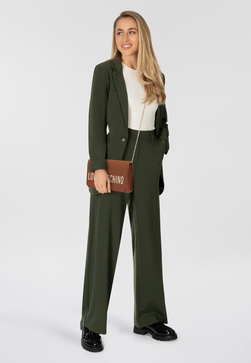 Olijfgroene op maat gemaakte pak met een ontspannen pasvorm, voorzien van een blazer met één knoop en brede broekspijpen; gecombineerd met een bruine schoudertas.