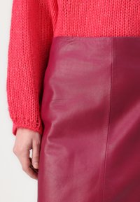 Rosa Lederrock mit glatter Textur und taillierter Silhouette; kombiniert mit einem knallpinken Strickpullover mit gerippten Bündchen.