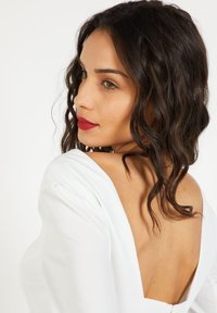 Vestido blanco con un profundo escote en la espalda, con mangas cortas y una textura suave y lisa. El cabello rizado oscuro y los labios rojos completan el conjunto.