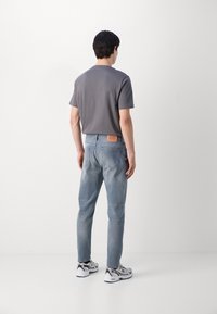 T-shirt en coton gris associé à un jean en denim bleu clair. Détails déchirés sur le jean, patch en cuir à la taille et baskets neutres.