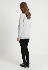 Sweat-shirt gris à coupe décontractée, manches longues et ourlet arrondi, associé à des leggings noirs et des bottines à garnitures argentées.