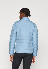 Giacca a vento blu chiaro con colletto alto, texture trapuntata orizzontale e silhouette aderente. Presenta maniche lunghe e orlo elasticizzato.