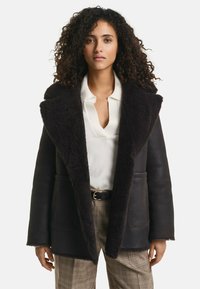 Zwarte leren jas met een fluffy zwarte schapenvacht kraag, voorzien van opgestikte zakken en een relaxte pasvorm, gecombineerd met geruite broeken.