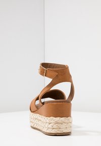 Bruine leren wedge sandalen met een gevlochten jute platform, voorzien van een verstelbare enkelband en een open achterkant.