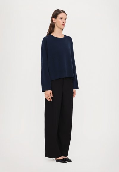 Navy blue cropped sweater with a round neckline and wide sleeves, paired with high-waisted black wide-leg trousers and black pointed shoes.