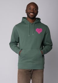 Groene hoodie met een voorzak, met een roze hartontwerp op de linker borst. Gemaakt van textuurstof met verstelbare koorden.