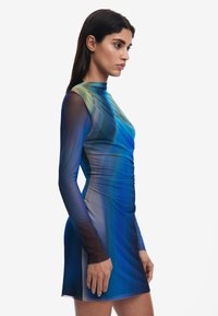 Långärmad klänning i gradientblå och grön genomskinlig material, med en figursydd siluett, hög hals och ruched-textur längs sidorna.