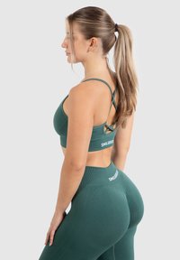 Sostenedor deportivo verde y leggings hechos de tela elástica. El sujetador cuenta con un diseño de espalda cruzada; los leggings tienen una cinturilla alta con logotipo.