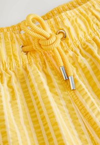 Tissu rayé jaune avec ceinture élastique froncée et cordon jaune tressé noué à travers des œillets métalliques.