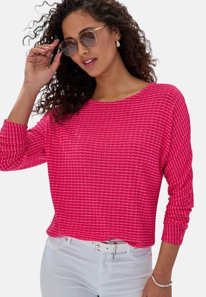 Fuchsia knit top with textured stripes, wide neckline, and long sleeves, paired with white jeans and sunglasses.