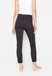 Jeans neri skinny con vita media, caratterizzati da una texture liscia, quattro tasche e dettagli di cucitura sottili.
