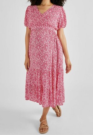 Robe maxi rouge à fleurs avec un décolleté en V, des manches courtes bouffantes, une taille empire, des volants froncés et un tissu doux. Associée à des sandales à lanières marron clair.