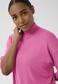 Rosa gestrickter Pullover mit hohem Kragen, weiter Passform und drei Viertel Ärmeln, mit glatter Textur und minimalistischem Design.