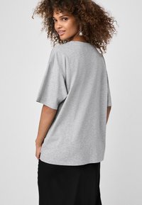 Grå oversized t-shirt med korte ærmer, rund halsudskæring og glat tekstur; båret sammen med en sort nederdel i en neutral baggrund.