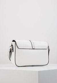 Vit syntetisk handväska med klaffstängning, svart kant och avtagbar rem. Har en slät yta och minimalistisk design.