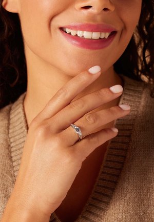 Solitaire engagement ring with a central round diamond, silver band, and side accents. Model displays the ring on her finger.