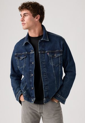 Dark blue denim jacket with a classic cut, button front, two chest pockets, and silver button accents. Pairing with a black shirt underneath.