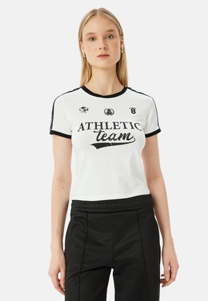 Korte mouwen witte t-shirt met zwarte geribbelde kraag en mouwen, met daarop een grafische opdruk en logo's van "ATHLETIC team" op de voorkant.