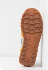 Semelle en caoutchouc d'une basket avec des crampons triangulaires en motif quadrillé, nom de marque visible, parties supérieures jaunes et grises.