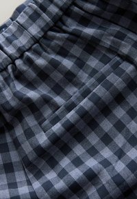 Geruite stof in marineblauw en grijs, met een geplooide tailleband en een zijzak. De textuur is glad met een lichte glans.