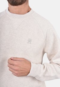 Felpa beige chiaro realizzata in tessuto texture con scollo rotondo, caratterizzata da maniche raglan e un piccolo logo ricamato sul petto.