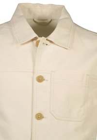 Beige bomullskappa med spetsig krage, fyra knappar och en bröstficka med klaff. Slät textur med synliga sömmar.