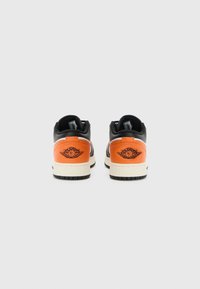 Sneakers neri e arancioni con una finitura in pelle liscia. Presentano un logo ricamato sul tallone e una suola di colore crema a contrasto.