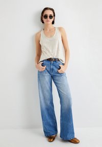 Beige paillet tanktop parret med lyseblå vidde jeans. Modellen bærer runde sorte solbriller og brune sko, samt et brunt bælte.