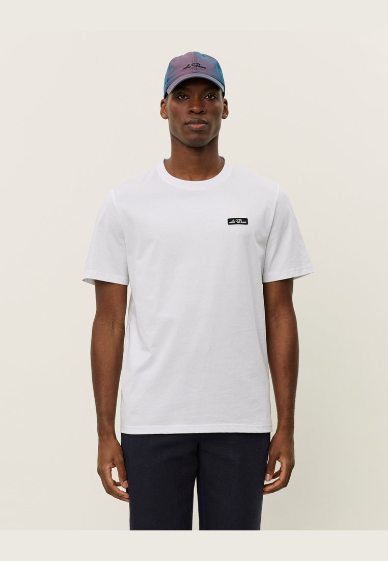 White cotton t-shirt featuring a small black logo tag on the left chest, paired with a multicolored cap with a logo on the front.