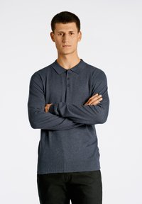 Marinblå långärmad polotröja med knäppt krage, tillverkad av textilerat tyg. Har en diskret logotyp på vänstra bröstet och ribbade ärmslut.