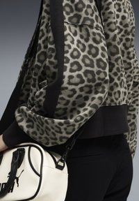 Felpa con stampa leopardata e bordi neri; tessuto morbido, vestibilità oversize. Borsa bianca con accenti neri e logo, tenuta da una tracolla.