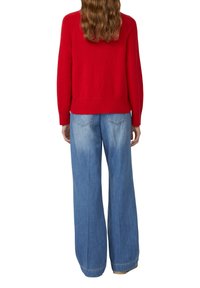 Czerwony sweter z dzianiny z prążkowanymi mankietami i dołem, zestawiony z jasnoniebieskimi spodniami typu wide-leg z tylnymi kieszeniami i lekko wyblakłym kolorem.