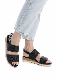 Sandali neri intrecciati con due fasce larghe, suola platform beige e una piccola fascetta alla caviglia. Superficie texturizzata e design open toe.
