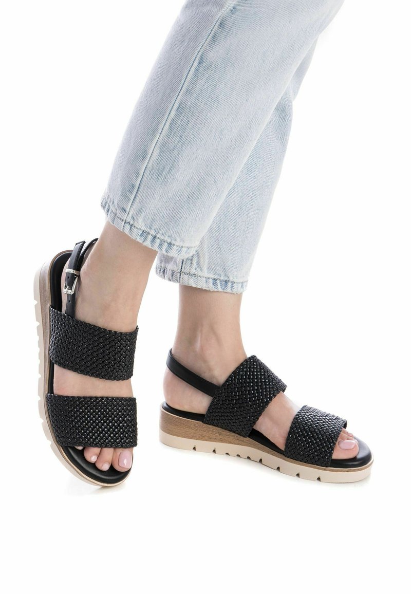 Sandali neri intrecciati con due fasce larghe, suola platform beige e una piccola fascetta alla caviglia. Superficie texturizzata e design open toe.