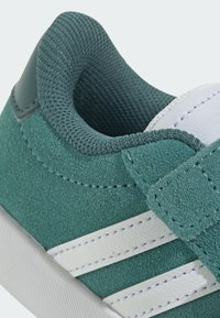 Teal semišové tenisky s bílými koženými pruhy, polstrovaným límcem a suchým zipem. Texturovaný povrch a zesílené švy.