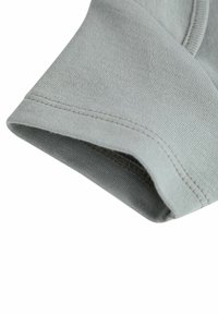 Tessuto di cotone grigio chiaro con una texture morbida. Presenta un polsino piegato con cucitura visibile. La vista ravvicinata mostra un fine motivo a righe.