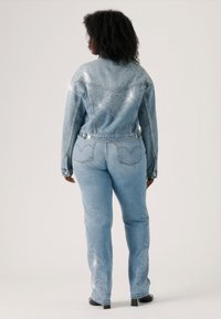 Veste en denim bleu clair et pantalon avec broderie au dos et clous décoratifs. Présente un design ajusté et une coupe classique de jean avec poches.