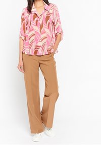 Blus med mönster i rosa och krämfärg, med lös passform och knappstängning framtill, tillsammans med breda byxor i tan och vita sneakers.