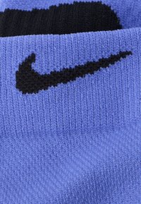 Μωβ βαμβακερή κάλτσα με ριμπ υφή, με μαύρο λογότυπο Nike. Η πάνω ταινία είναι μαύρη με αντίθετο μωβ κάτω τμήμα.