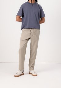 Casual outfit met een marineblauw T-shirt met korte mouwen, beige broek met trekkoord, en witte sneakers met donkere accenten en een gumkleurige zool.