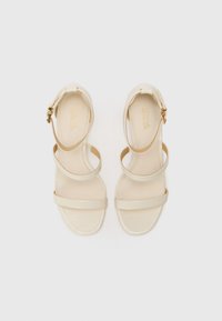 Sandali in pelle beige con cinturini, tre fasce sottili sopra il piede, una fascia anteriore ampia e una fibbia dorata sul cinturino alla caviglia. Suola piatta.
